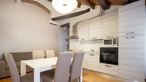 A modern kitchen with white cabinets, a built-in microwave, and an oven. There is a dining table with chairs and a sofa in the adjacent living area. - Herion Palace Apt. 2 by Wonderful Italy (Venecia)