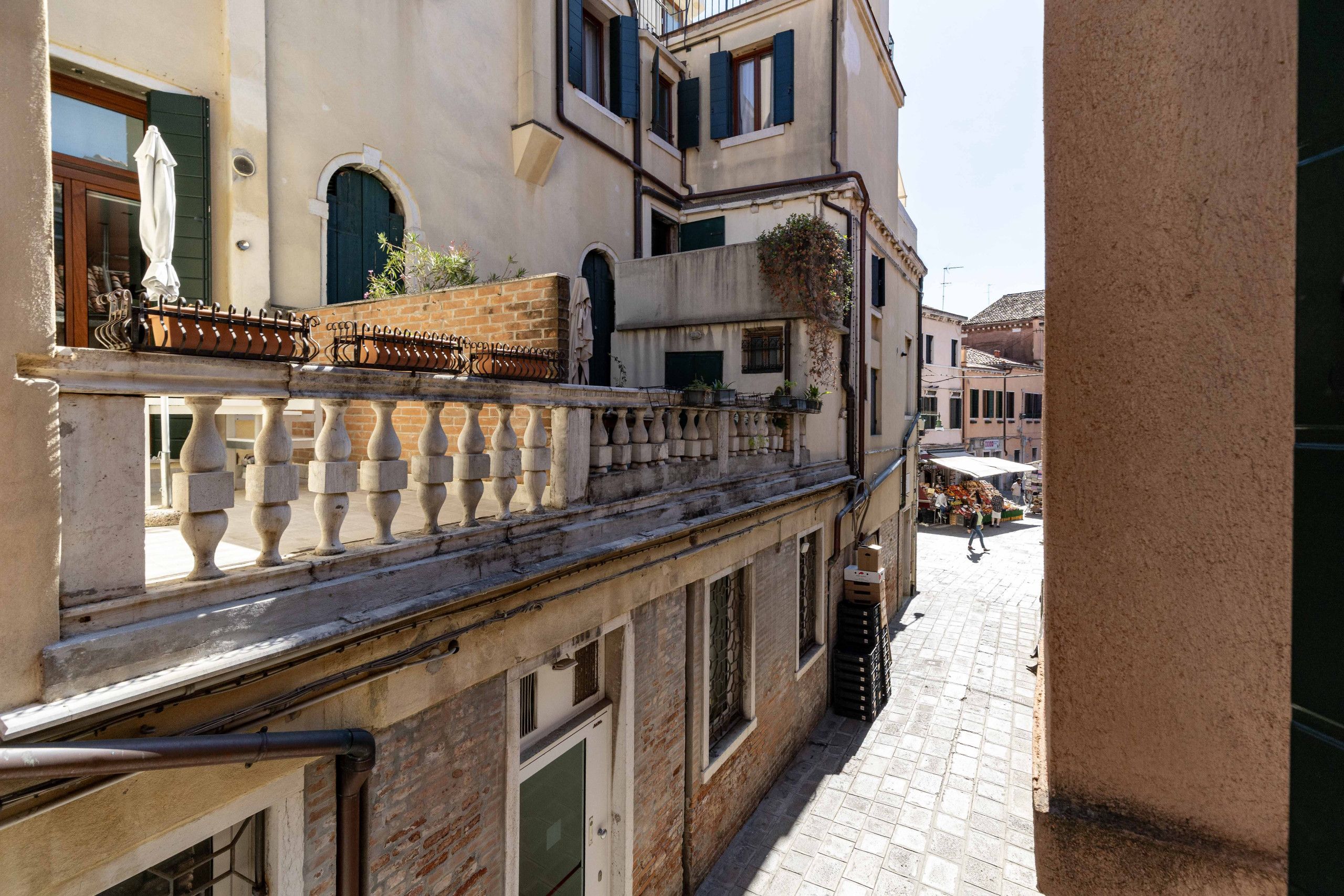 Una stretta via fiancheggiata da edifici con balconi, un pavimento in piastrelle e un cielo sereno.