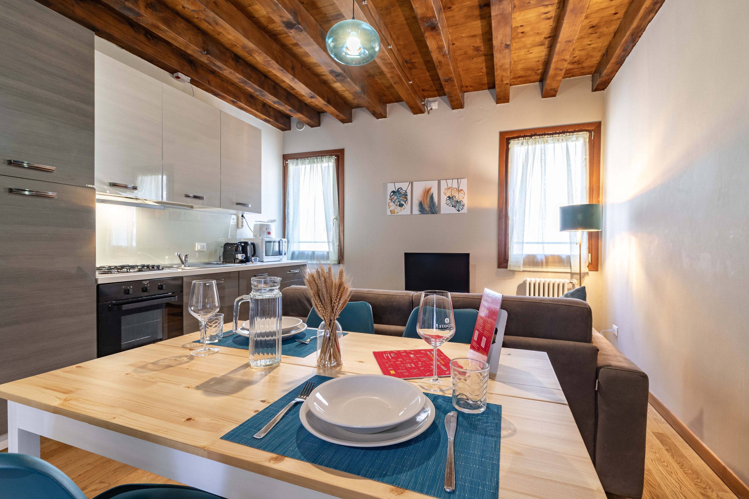 Una cucina moderna con zona pranzo, travi a vista in legno e vista sul soggiorno.
