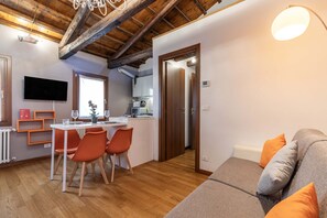 A modern living room with a wooden ceiling, a dining area with orange chairs, and a kitchen with a TV and a plant. - Herion Palace Apt. 5 by Wonderful Italy (Venecia)