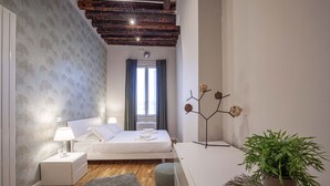 A bedroom with a bed, bedside table, lamp, potted plant, and a decorative wall piece.