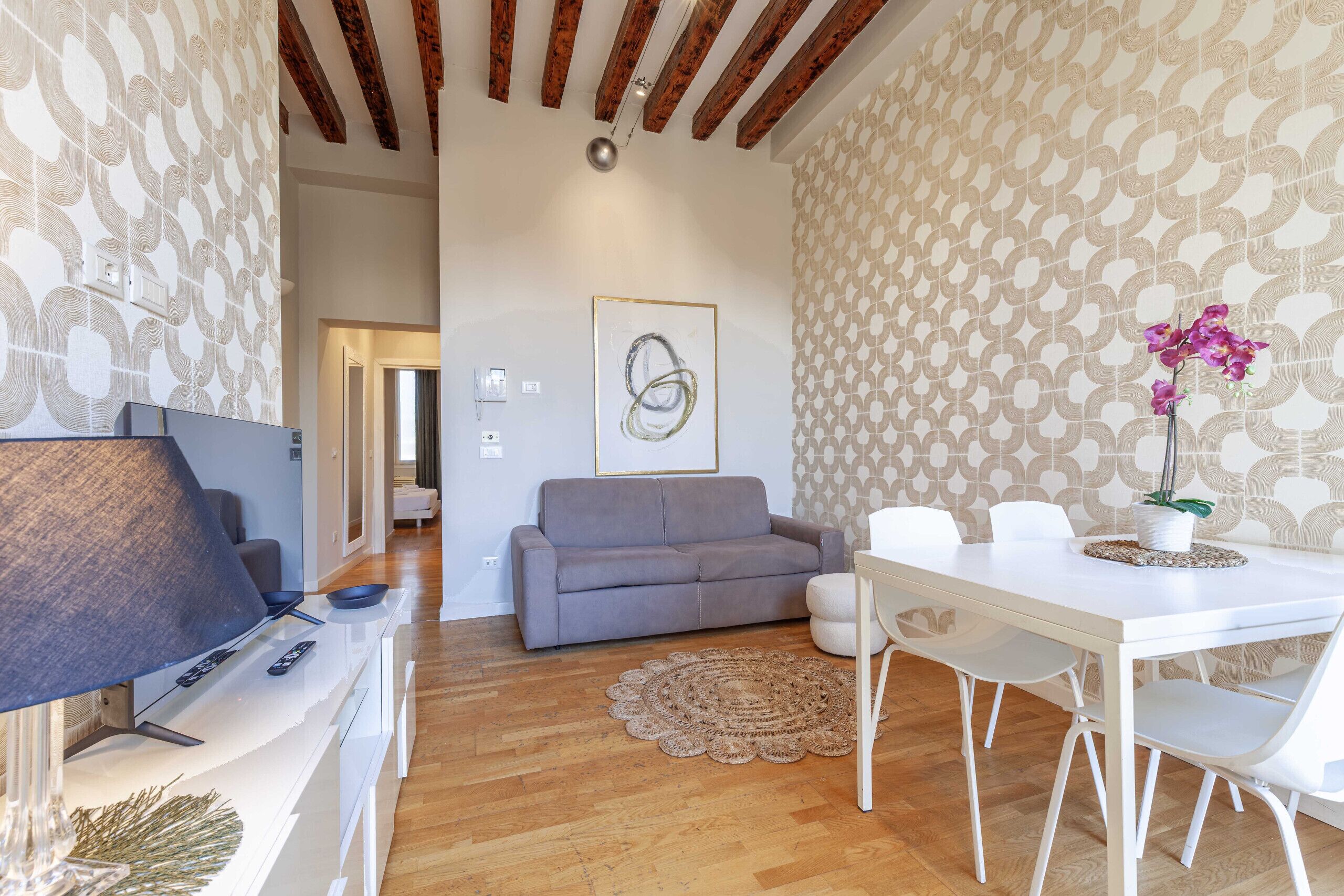 Ein modernes Wohnzimmer mit einem grauen Sofa, einem weißen Esstisch und einem dekorativen Teppich.