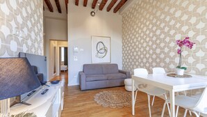 A modern living room with a grey sofa, white dining table, and a decorative rug.
