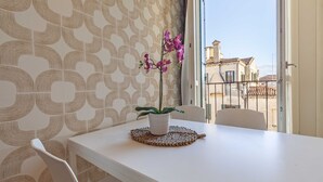 A room with a patterned wallpaper, a potted orchid on a woven placemat, and a view of buildings through a window.