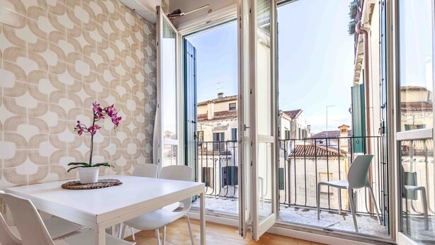 A modern interior with a white table and chairs, a potted orchid, and a balcony with a metal railing.