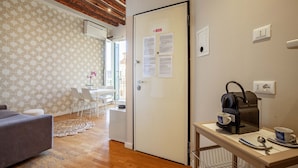 A room with a wooden ceiling, a white door with papers, a table with a coffee maker, and a patterned rug.