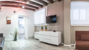 Ein modernes Wohnzimmer mit einem weißen Sofa, einem braunen Sofa, einer weißen Vitrine mit Pflanzen, einem Flachbildfernseher und einer Holzbalkendecke.