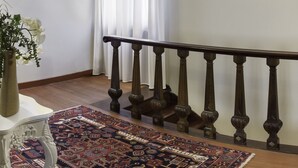 Une pièce avec un escalier, un tapis à motifs, un vase de fleurs et un luminaire fixé au mur.