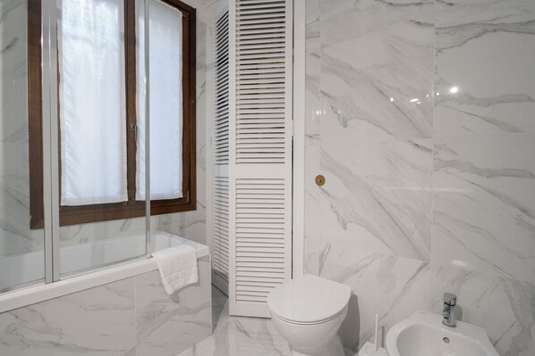 Un baño con inodoro, bidé y cabina de ducha acristalada.