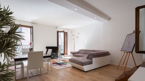 A modern living room with a sofa, a dining table, chairs, a TV, and an easel with a painting. - San Marco Square With Terrace by Wonderful Italy (Venecia)