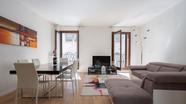 A modern living room with a dining area, a sofa, a TV, and a balcony with a railing. - San Marco Square With Terrace by Wonderful Italy (Venecia)