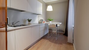Une cuisine moderne avec des meubles blancs, un évier en acier inoxydable, une bouilloire et une plante en pot.