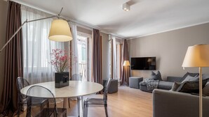 A modern living room with a round dining table, clear chairs, a grey sofa, and a flat-screen TV mounted on the wall. - San Marco Suite 2 by Wonderful Italy (Venecia)