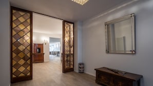 Un couloir doté d’un plancher en bois, d’un banc en bois, d’un miroir au mur et d’une porte ornée d’un panneau de verre décoratif.