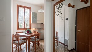 A kitchen with wooden cabinets, a dining table with chairs, and a window with curtains. - Venice Grand Canal Style Apt. 2 by Wonderful Italy (Venecia)