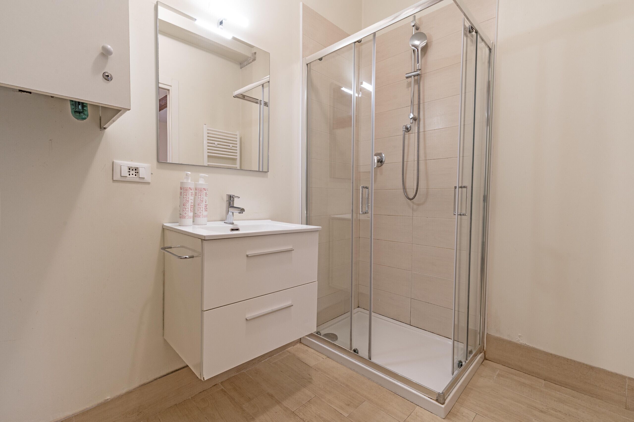Une salle de bain moderne avec une douche à parois de verre, un meuble-lavabo blanc doté de tiroirs et un miroir au-dessus du lavabo.