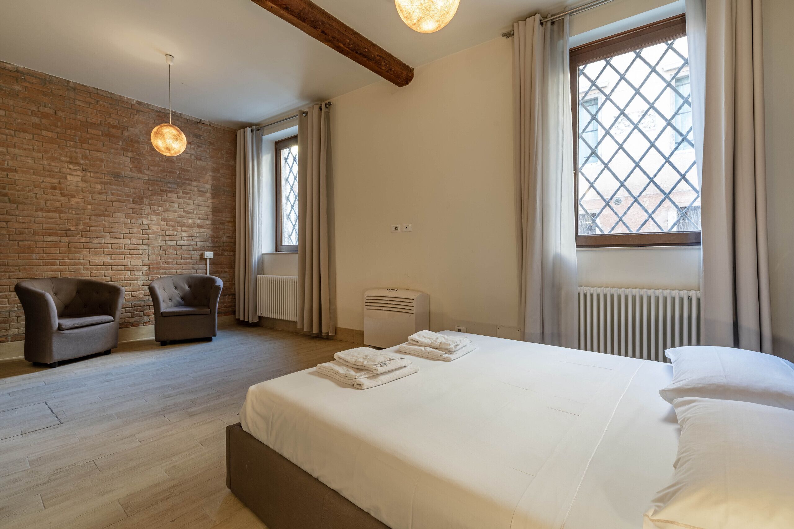 Un dormitorio con una cama grande, una silla, un radiador y una ventana con cortinas.