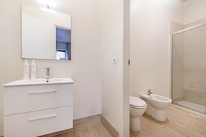 A bathroom with a white vanity, a mirror, a toilet, and a bidet.