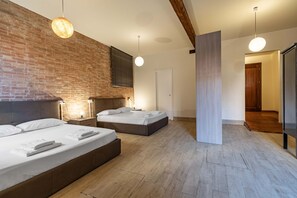 A modern hotel room with a brick wall, two beds, a wooden floor, and pendant lighting.