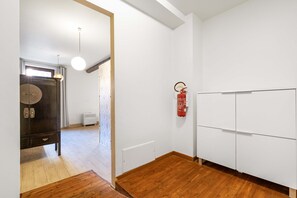 A room with a wooden floor, white walls, a wardrobe, a hanging light fixture, and a fire extinguisher mounted on the wall. - Venice Luxury Palace 1 by Wonderful Italy (Venecia)