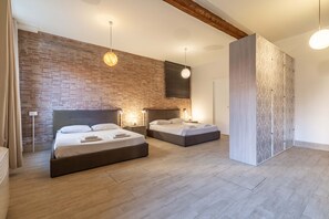 A modern bedroom with two beds, a brick wall, wooden beams, and a large wardrobe.