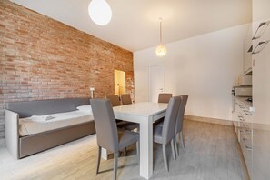 A modern interior with a brick wall, a white dining table with chairs, a sofa, and a kitchen area.