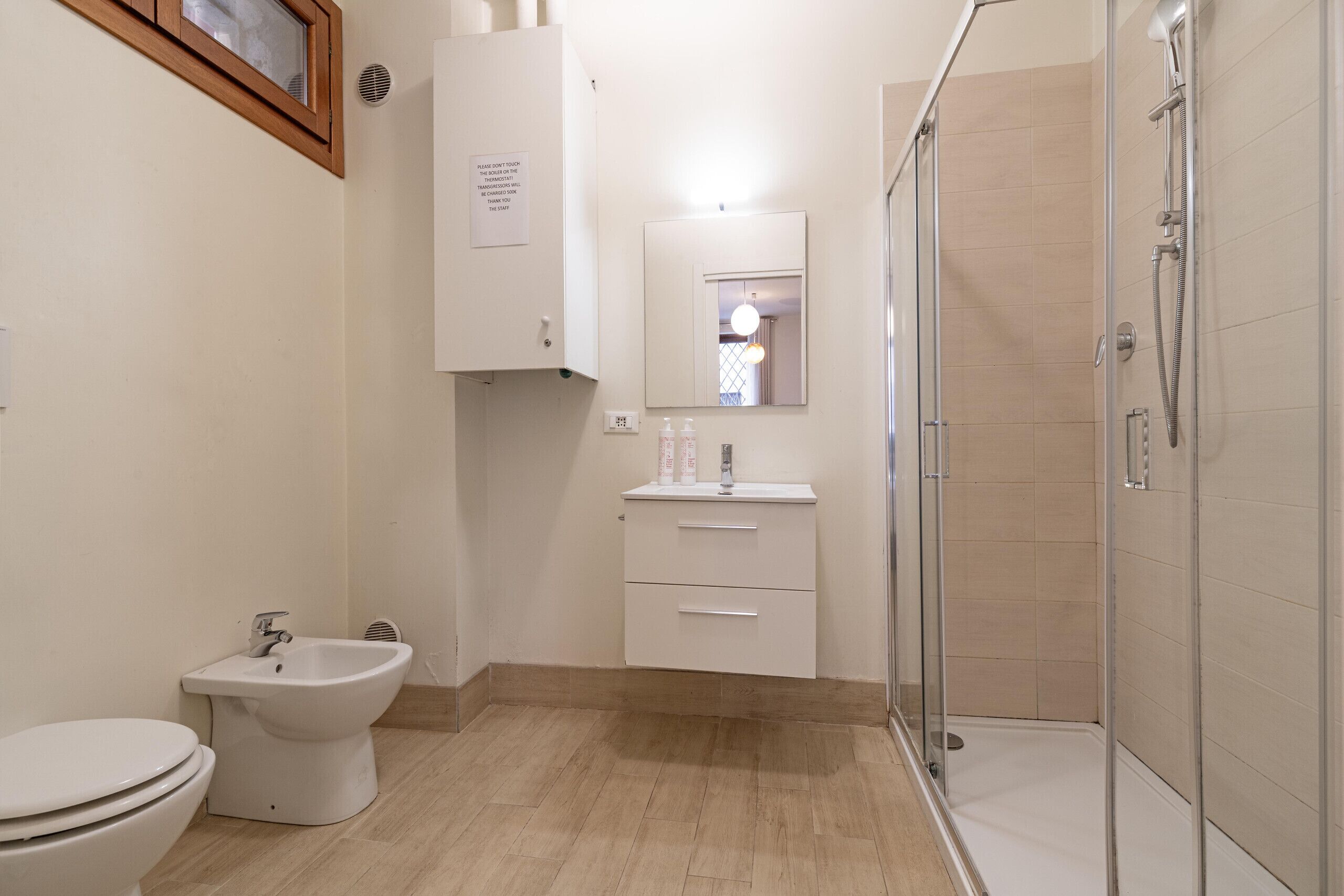 Une salle de bain comprenant des toilettes, un bidet, un lavabo, un miroir et une douche fermée par une paroi de verre.
