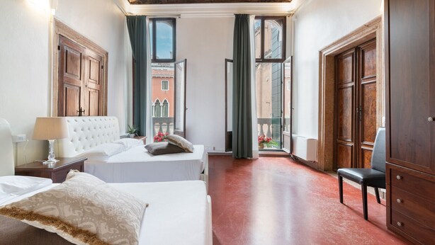 A hotel room with a bed, a chair, a desk, and a view of the outside. - Venice Luxury Palace 3 by Wonderful Italy (Venecia)