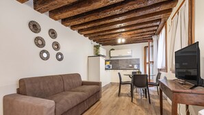 Una sala de estar acogedora con un sofá marrón, vigas de madera en el techo y un televisor sobre una mesa de madera.