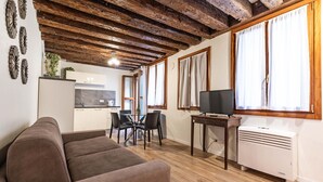 Una sala de estar con un sofá marrón, una mesa de comedor con sillas, un televisor sobre un mueble bajo y un aire acondicionado blanco.