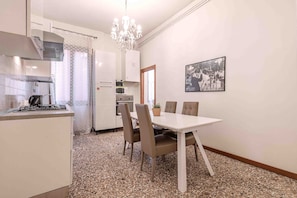 Cozinha compacta com fogão a gás, micro-ondas e frigorífico. Possui uma mesa de jantar com cadeiras e um candelabro.