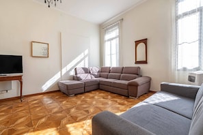 Sala de estar com sofá seccional, televisão e piso estampado.
