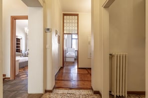 Corredor com piso de madeira, um radiador e uma cama ao fundo.
