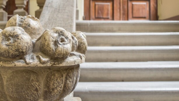 Una estatua de león de piedra a la base de una escalera que conduce a una puerta de madera con un arco decorativo encima.