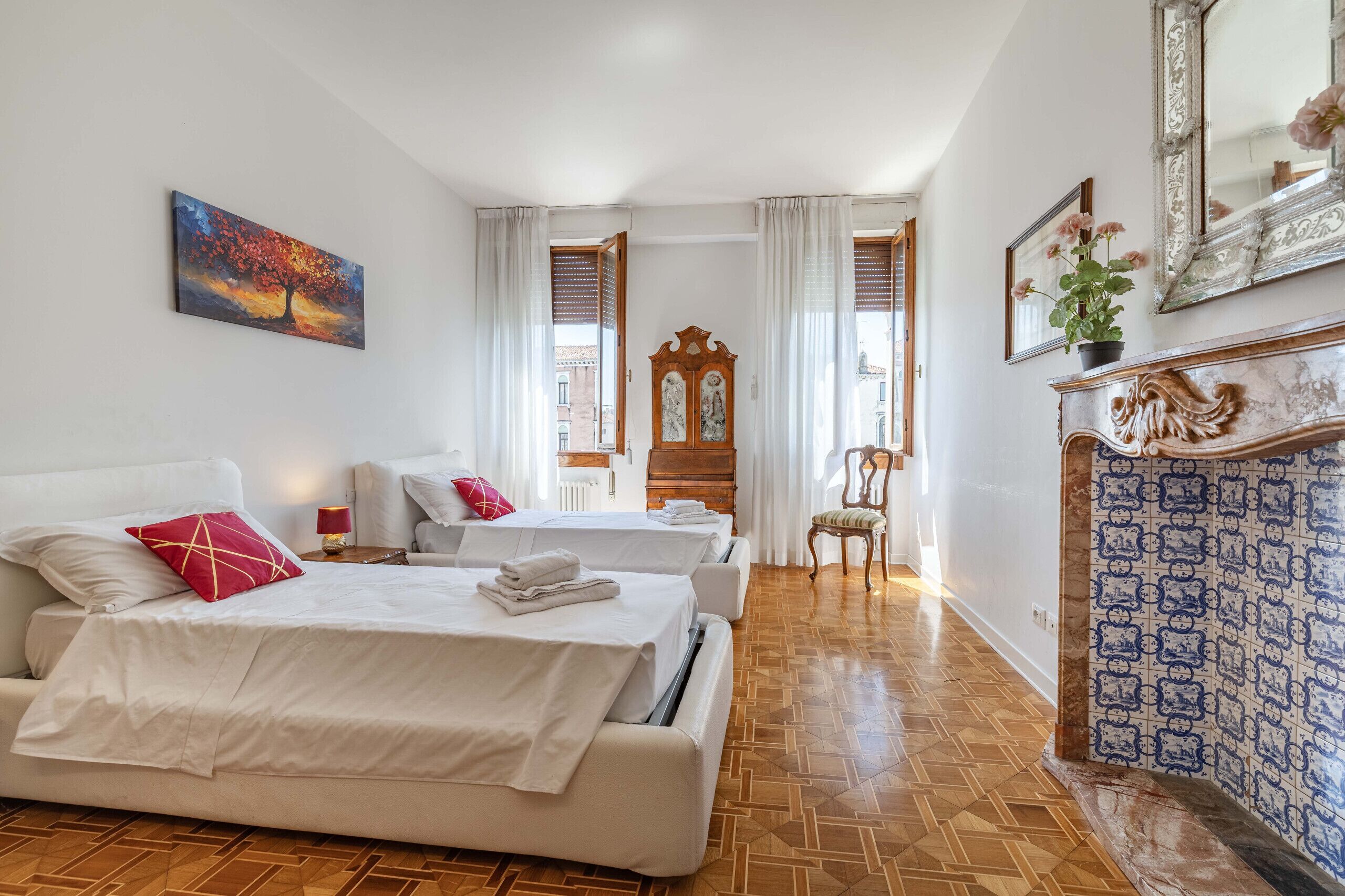 Een hotelkamer met twee bedden, een houten vloer, een grote spiegel en uitzicht op de straat.