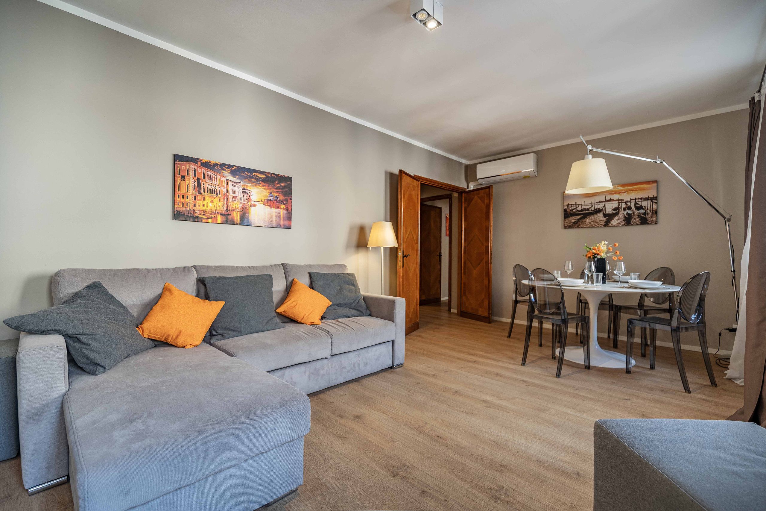 Ein modernes Wohnzimmer mit einem grauen Sofa, einem Esstisch mit Stühlen und Bildern an der Wand.