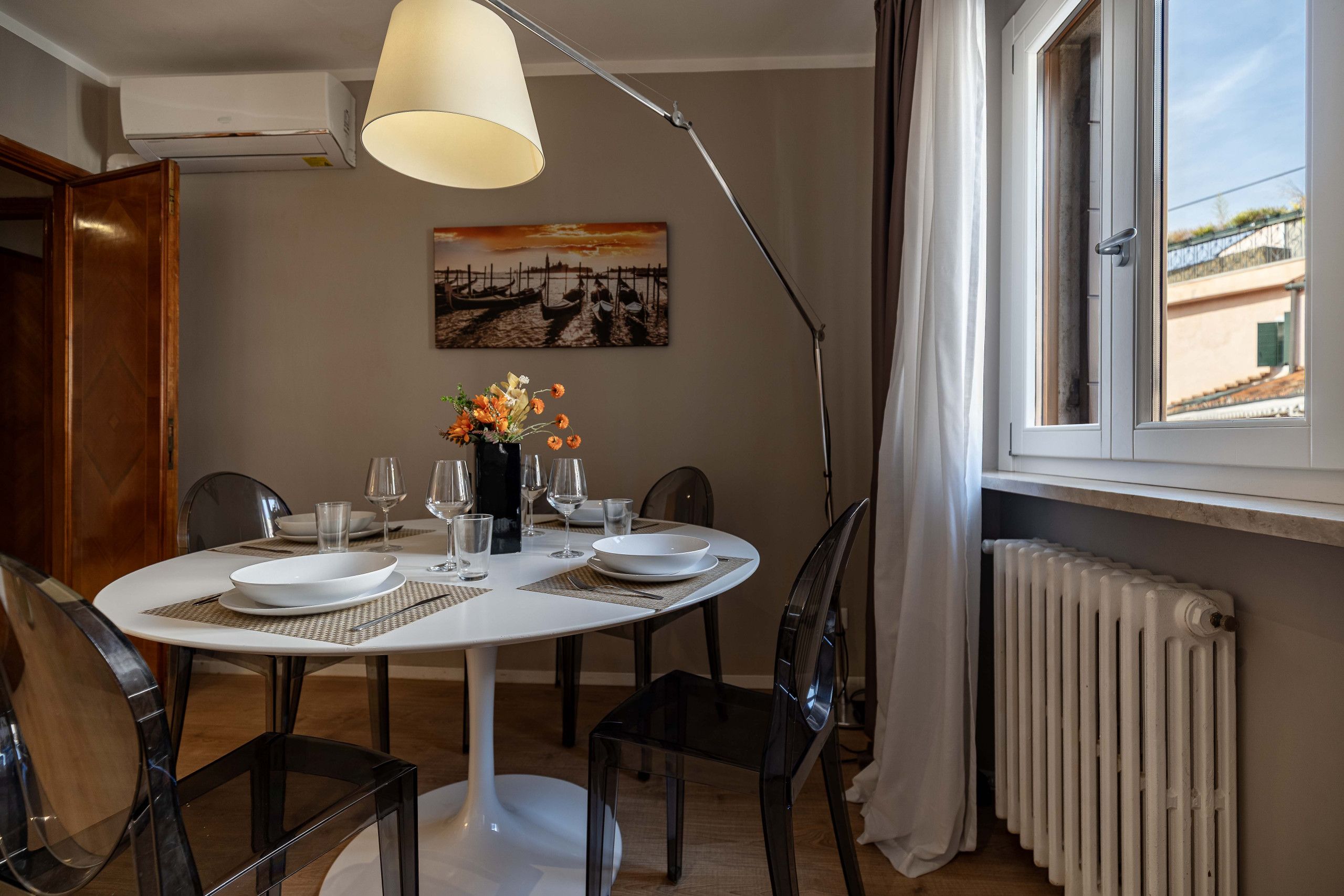 Ein Essbereich mit einem runden Tisch, gedeckt für vier Personen, einer Blumenvase und einem Bild an der Wand.