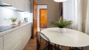 Une cuisine moderne avec des armoires blanches, un comptoir noir et une table à manger blanche avec des chaises. On aperçoit une plante en pot sur la table et, au fond, une fenêtre avec des rideaux.