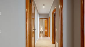 Un couloir avec des portes en bois et un plancher de couleur claire, qui mène à une pièce éclairée par une lampe.