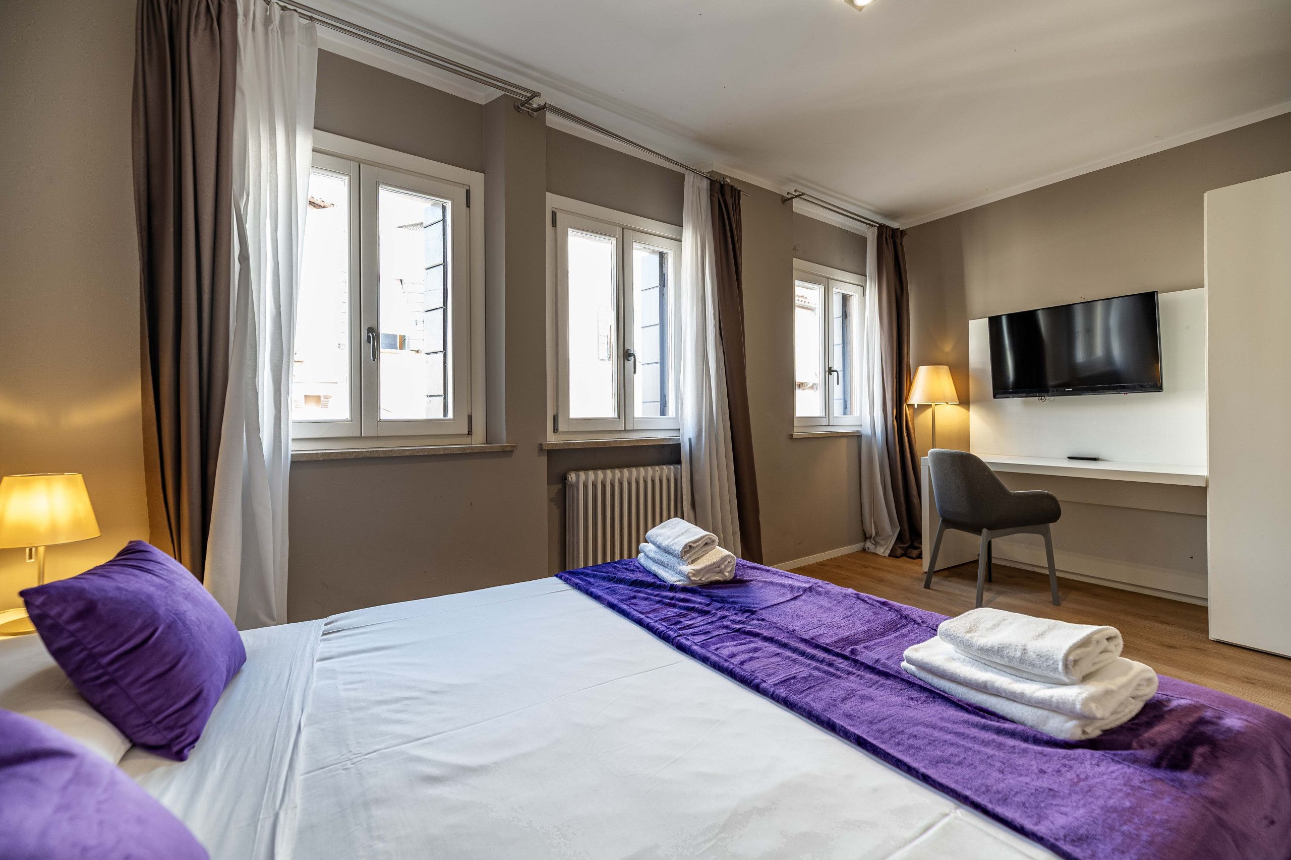 Ein Hotelzimmer mit einem Bett, einem Schreibtisch, einem Sessel, einem Fernseher und einem Fenster mit Vorhängen.