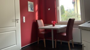 A dining area with a table and chairs, a vase with flowers, a painting on the wall, and a window with a view of greenery.