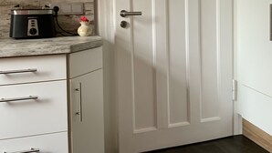 A kitchen with white cabinets, a white door, and a countertop with a rice cooker and a vase.