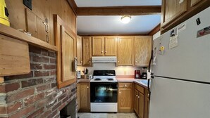 A kitchen with wooden cabinets, a brick wall, a stove, and a refrigerator. - 3BR/1BA Eastham cottage w/ backyard, A/C & WiFi (Eastham)