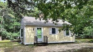 A small, single-story house with a green door and white shutters, surrounded by trees and a grassy yard. - 3BR/1BA Eastham cottage w/ backyard, A/C & WiFi (Eastham)