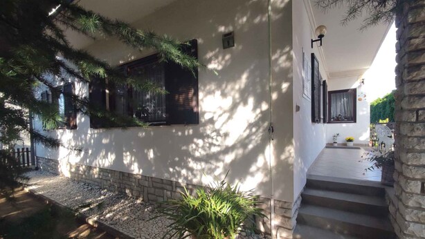 A house with a stone staircase leading to a porch, a small garden with a potted plant, and a wooden fence. - Holiday home with wifi and air conditioning (Balatonboglár)