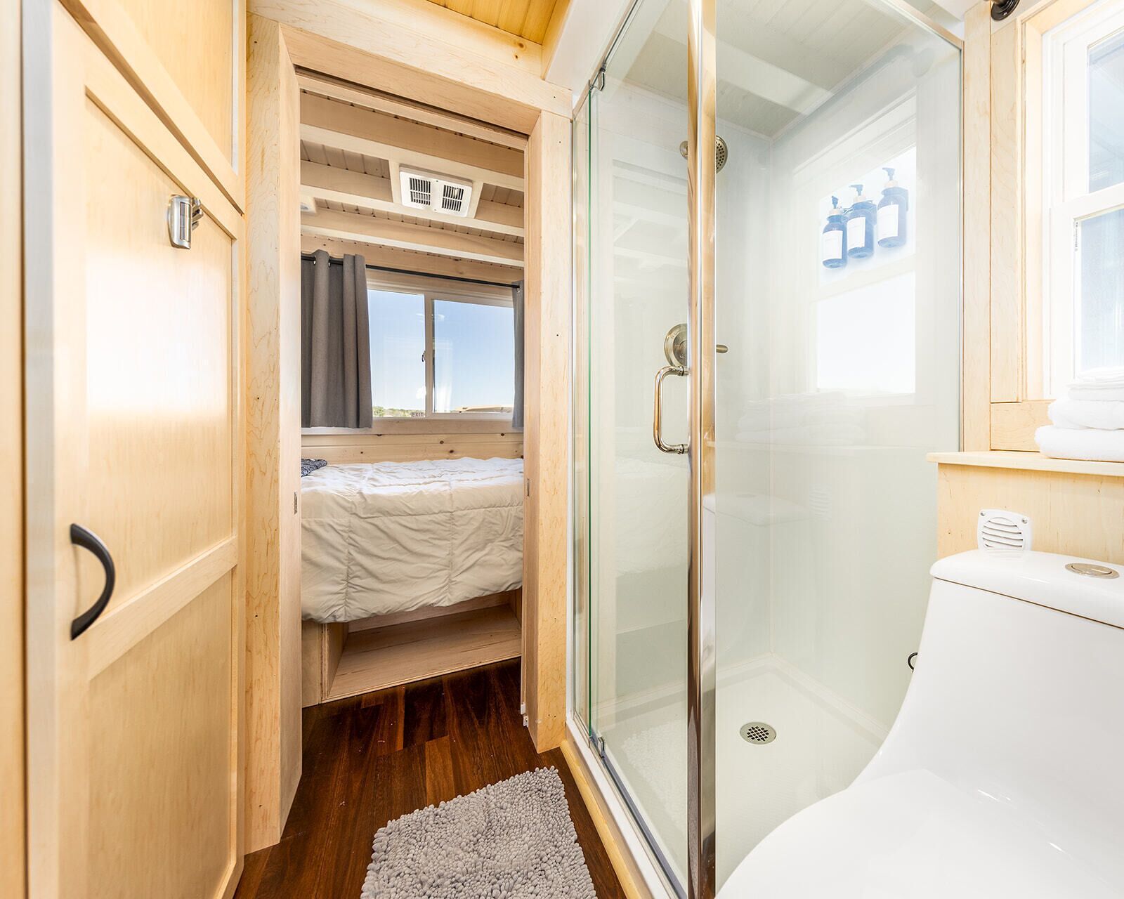 A compact RV bedroom with a bed, a shower stall, and a toilet.