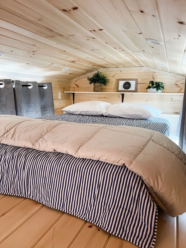 Une chambre dans une cabane en bois, avec deux lits, un ventilateur de plafond et une petite étagère ornée de plantes.