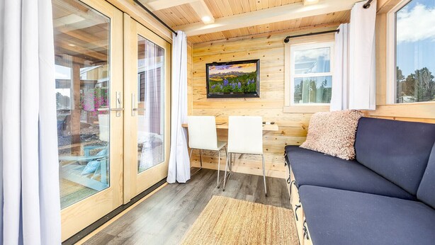 Interior acollidor d'una cabana amb sostre de fusta, un sofà, una televisió i una zona de menjador.