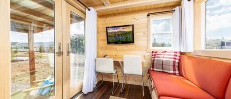 Interior acollidor d'una cabana amb sostre de fusta, un televisor penjat a la paret, un sofà i zona de menjador amb dues cadires.