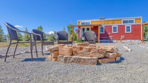 A red cabin with a porch and two wicker chairs. - Luxury Tiny Home/Base Camp to Ouray, Telluride/3 Queen beds/Washer & Dryer/Smart TV/Hot Tub Access/Patio w/Mountain Views/ Fire Pit/11 mi to Airport (Montrose)